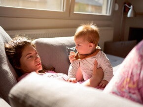 Woman lying on the couch in pyjamas with baby on her lap