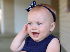 Baby in blue dress crying and pulling on ear